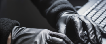 A person wearing black gloves typing something on a computer